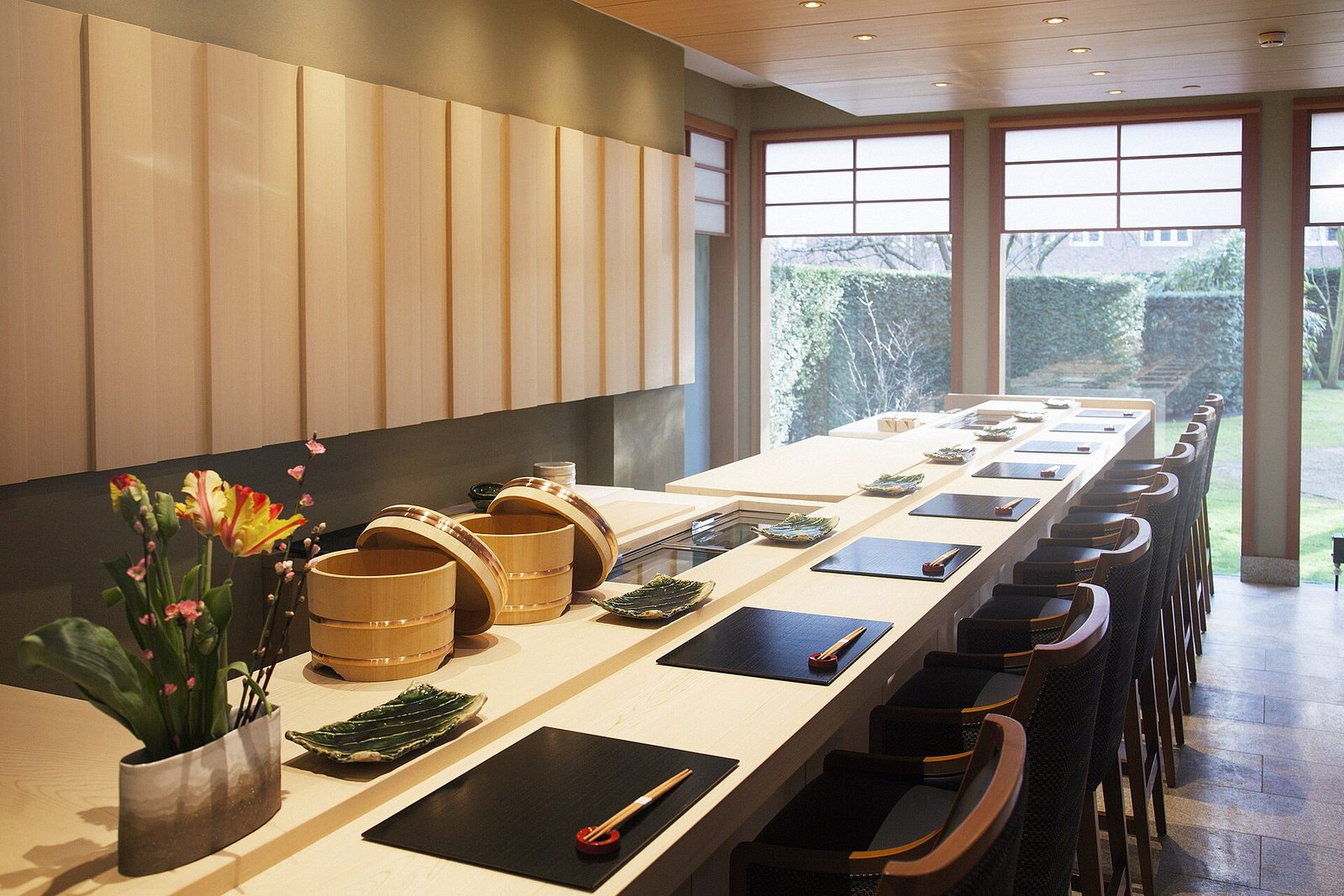 An empty sushi counter with chairs, placemats, and wooden rice tubs